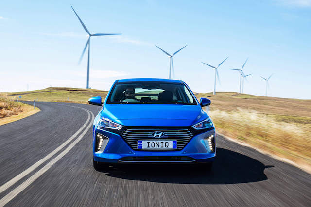 Electric vehicle Hyundai Ioniq Hybrid being driven with wind turbines in the background