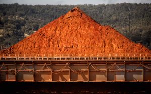 Large earthy red mound of ground bauxite in the sunshine at an alumina refinery.