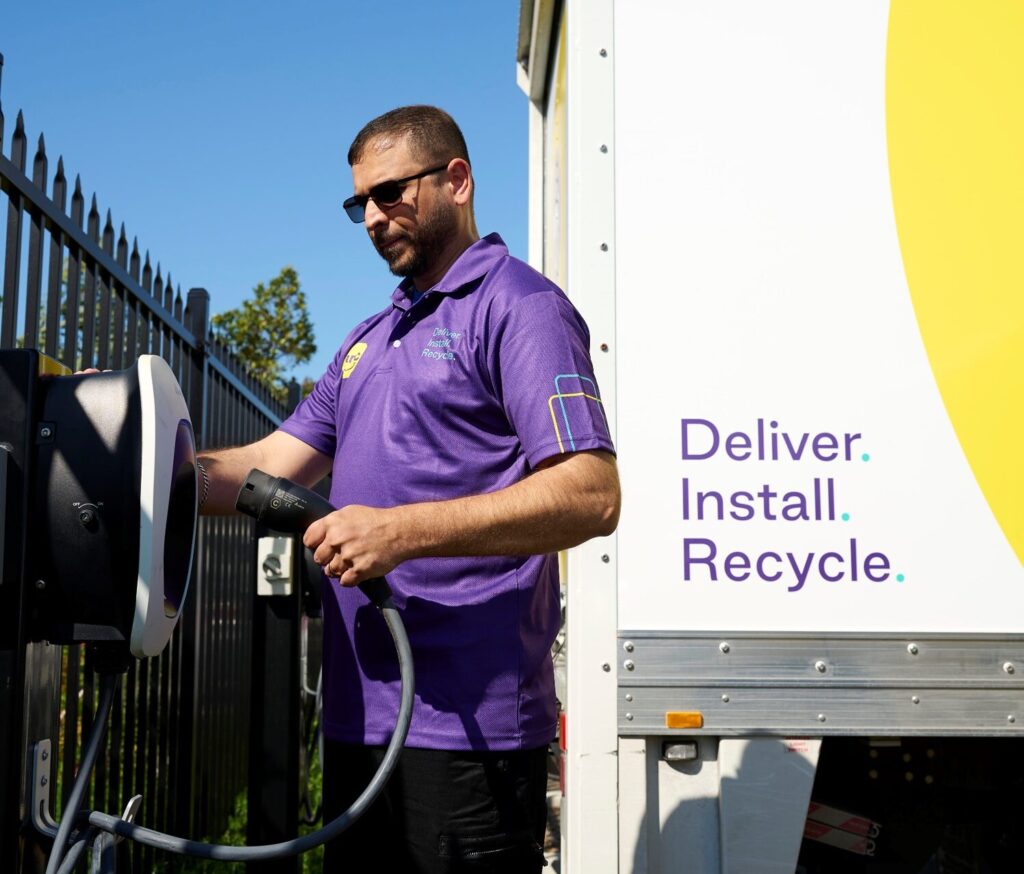 A man in a purple shirt plugs an electric truck into a charging point.